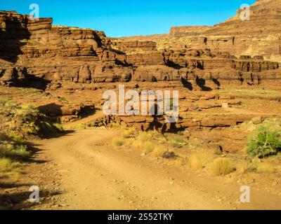 Una strada sterrata si snoda attraverso un canyon roccioso. La strada è stretta e tortuosa, e il canyon è pieno di rocce e massi. Il cielo è limpido e blu, e. Foto Stock