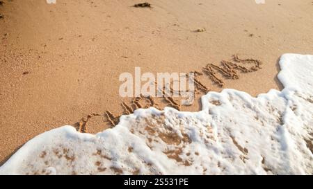 Immagine ravvicinata delle onde del mare che rotolano sopra la parola Natale scritta sulla sabbia bagnata. Concetto di vacanze invernali, Capodanno e turismo. Foto ravvicinata del mare Foto Stock