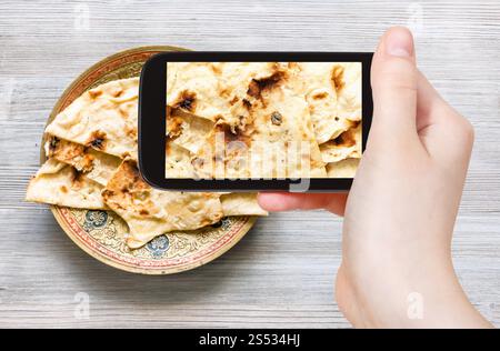 Concetto di viaggio - visitatore fotografie di cucina indiana di Naan pane piatto cotte nel forno tandoor sulla lastra di ottone sullo smartphone Foto Stock