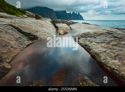 La spiaggia sassosa con bagni di marea a Ersfjord, Senja, Norvegia. Estate giorno polare notte costa. I denti di drago di roccia nel lontano. Foto Stock