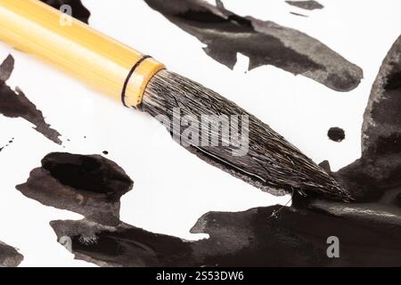 Tinto nero round pelo di capra punta del pennello di bambù per sumi-e ( suibokuga) pittura su macchie di inchiostro sulla carta bianca close up Foto Stock