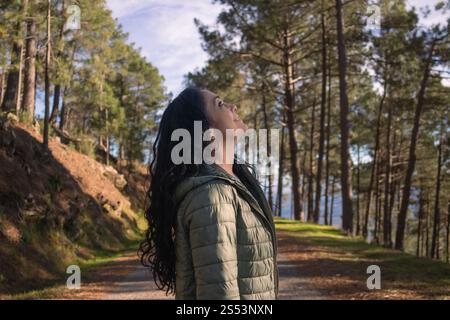 Bruna dai capelli lunghi che sorride e guarda il cielo in una pineta Foto Stock