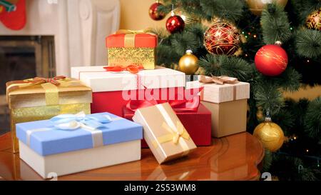 Bella foto di molti regali e regali per Natale sdraiati su un tavolo di legno nel soggiorno della casa contro ghirlande e baubles Chrismtas. Foto Stock