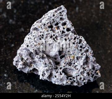 primo piano di un campione di minerale naturale proveniente dalla collezione geologica - roccia di pomice nera ruvida su sfondo di granito nero. Ruvida pietra pomice nera Foto Stock