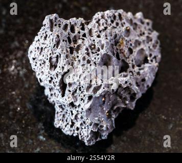 primo piano di un campione di minerale naturale proveniente dalla collezione geologica - pietra pomice nera non lucidata su fondo di granito nero. Pomice nera non lucida Foto Stock