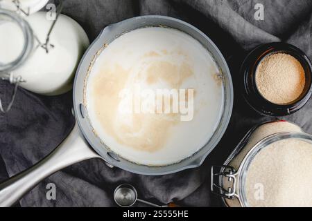 Vista ravvicinata della prova del lievito nel latte riscaldato: Direttamente sopra il lievito protetto in una pentola con altri ingredienti per il pane e utensili da cucina Foto Stock