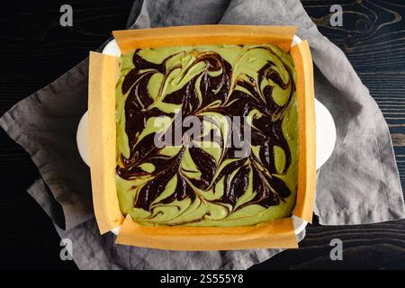 Pastella di brownie Matcha Cheesecake mescolata nel piatto da forno: Brownie al cioccolato fondente non cotti al forno e formaggio cremoso al tè verde in una teglia da forno in ceramica Foto Stock