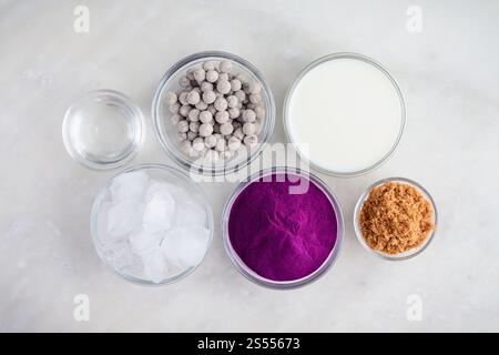 Ingredienti per il tè Bubble Purple Sweet Potato: Patate dolci in polvere, polpette di tapioca e altri ingredienti su un tavolo di marmo bianco Foto Stock