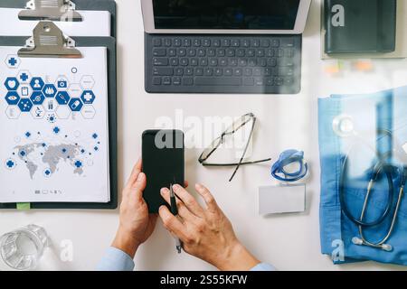 vista dall'alto del medico intelligente che lavora con il telefono cellulare, il computer portatile e lo stetoscopio su una scrivania di legno scuro Foto Stock