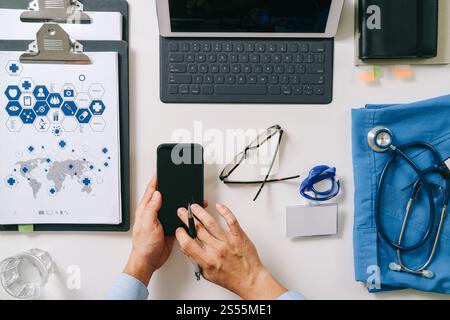 vista dall'alto del medico intelligente che lavora con il telefono cellulare, il computer portatile e lo stetoscopio su una scrivania di legno scuro Foto Stock