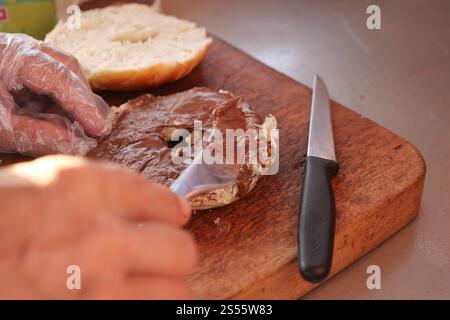 Spalmare uno strato cremoso di cioccolato su un bagel fresco con un coltello Foto Stock
