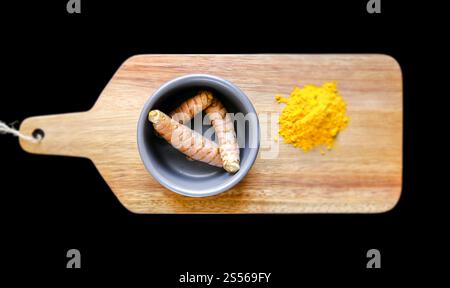 Radice di curcuma nel recipiente e polvere di spezie su un tagliere di legno. Isolato su sfondo nero. Radice di curcuma nel recipiente e polvere di spezie su un taglio Foto Stock