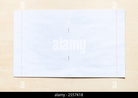 vista dall'alto di un quaderno vuoto aperto con fogli quadrati con margini su asse di legno marrone chiaro Foto Stock