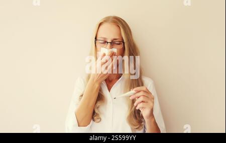 Malato turbato dipendente donna caucasica starnuti colpo naso utilizzando il tessuto e misurare la temperatura corporea guardando il termometro a casa Foto Stock