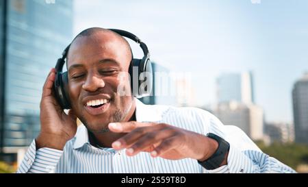 Uomo d'affari felice che si rilassa all'aperto ascoltando musica con le cuffie in una giornata di sole Foto Stock