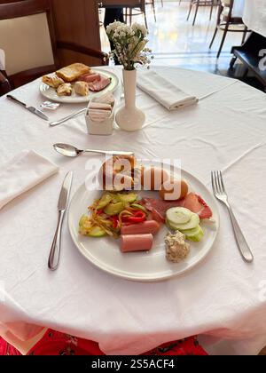 Tavolo per la colazione organizzato con una varietà di cibi su una tovaglia bianca in un ambiente raffinato. Colazione in hotel, pasti mattutini Foto Stock