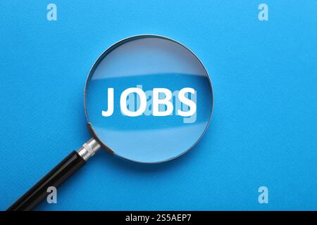 Concetto di ricerca lavoro. Parola su sfondo blu, vista tramite lente di ingrandimento Foto Stock