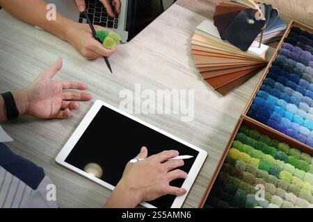 vista dall'alto di due colleghi interior designer che discutono i dati con un tablet digitale e un nuovo computer portatile moderno con un campione di materiale su una scrivania in legno Foto Stock