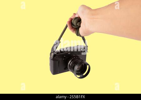 Mano maschio che tiene una fotocamera digitale telemetrica isolata su sfondo giallo. Foto Stock