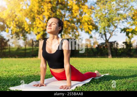 Donna caucasica che pratica yoga su un tappetino in un parco cittadino. Yoga mattutino. Foto Stock