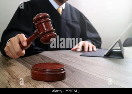 La giustizia e la nozione di diritto.Giudice maschi nelle aule di un tribunale che colpisce il martello,lavora con tavoletta digitale computer tastiera docking sulla tavola di legno Foto Stock