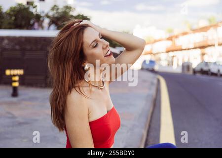Una donna con un vestito rosso siede sul marciapiede, sorride e guarda il cielo. Foto Stock