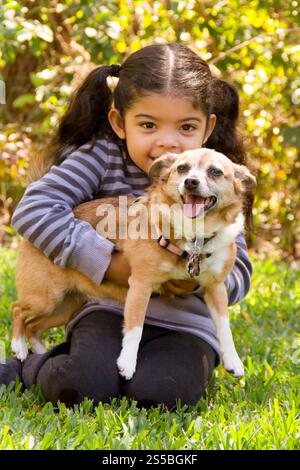 Sorridente ragazza seduta su un prato in estate coccolando il suo cane terrier domestico Foto Stock