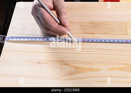 vista frontale della mano di carpentiere con matita misura lunghezza su legno asse con nastro di misura in primo piano Foto Stock