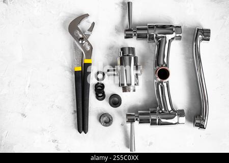 fondo idraulico - vista dall'alto della chiave, valvola del rubinetto della doccia smontata, deviatore, beccuccio, guarnizioni su tavola di cemento con copyspace Foto Stock