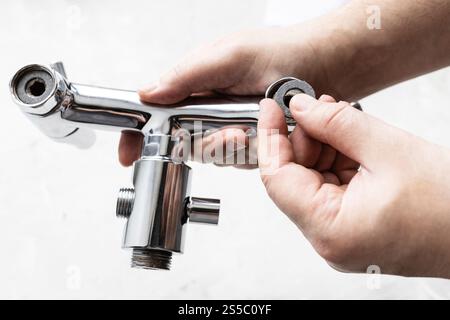 l'idraulico installa la guarnizione paronite nel chioseup del rubinetto della doccia e il pannello di calcestruzzo grigio sullo sfondo Foto Stock