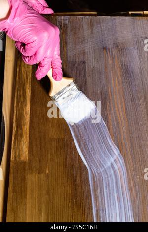 la mano gloved vernicie un asse macchiato della mobilia del pino in casa Foto Stock