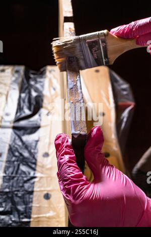 vernici a mano con guanti con spazzola l'estremità del pannello di legno si avvicina al banco da lavoro a casa Foto Stock
