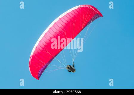 Un vivace parapendio rosso si libra attraverso il cielo azzurro. Foto Stock