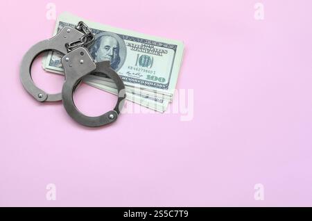 Le manette della polizia e centinaia di dollari giacciono su uno sfondo di colore corallo vivo. Il concetto di punizione per aver infranto la legge in campo finanziario Foto Stock