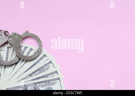 Le manette della polizia e centinaia di dollari giacciono su uno sfondo di colore corallo vivo. Il concetto di punizione per aver infranto la legge in campo finanziario Foto Stock