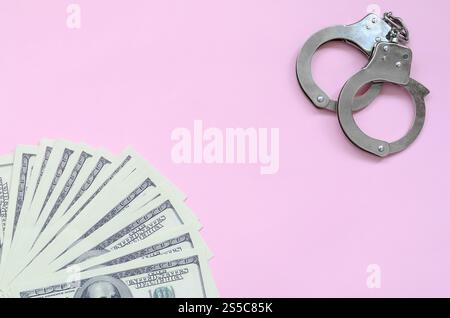 Le manette della polizia e centinaia di dollari giacciono su uno sfondo di colore corallo vivo. Il concetto di punizione per aver infranto la legge in campo finanziario Foto Stock
