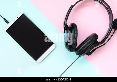 Le cuffie e lo smartphone neri si trovano su un colorato sfondo viola pastello. Concetto di ascolto musicale. Tecnologia portatile. Vista dall'alto in posizione piatta. Nero Foto Stock