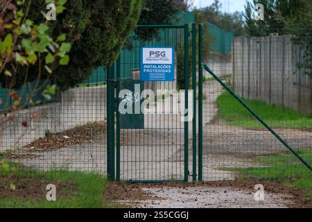 Cancello metallico verde chiuso con un cartello di sicurezza che indica le installazioni protette in portoghese Foto Stock