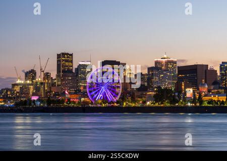 Il vecchio porto di Montreal e lo skyline del centro cittadino di notte. Edifici colorati che si riflettono nell'acqua. Montreal, Quebec, Canada. Ruota panoramica. Foto Stock