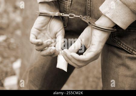 Arrestato spacciatore in manette con piccolo pacchetto di eroina su sfondo scuro. Concetto di traffico illegale di droga. Arrestato trafficante di droga Foto Stock
