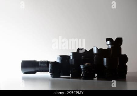 Molti obiettivi diversi per fotocamere reflex si trovano su una scrivania incolore. Immagine di sfondo per un biglietto da visita di un fotografo o di un fornitore di attrezzature fotografiche. Foto Stock