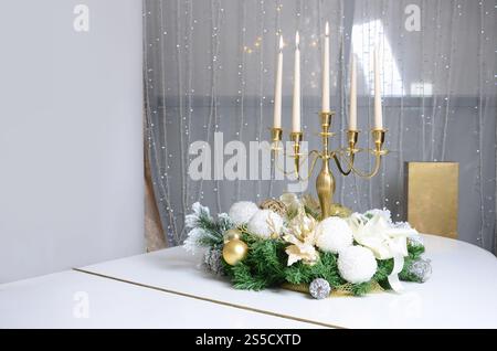 Decorazioni per il capodanno e un candelabro dorato con candele accese si stagliano sulla superficie di un pianoforte a coda bianco Foto Stock