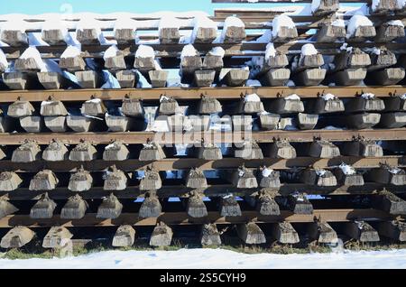 Molti vecchi binari e traversine sono impilati in un magazzino ferroviario in inverno. Il concetto di rinnovamento di una ferrovia logora Foto Stock