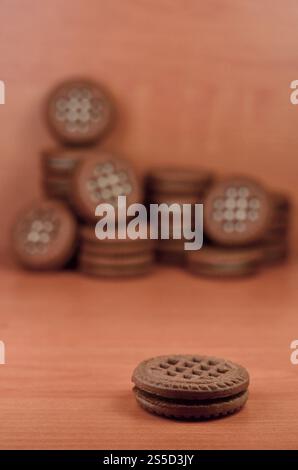 Un mucchio di biscotti con scaglie di cioccolato ripieni di crema bianca alla vaniglia giace su una superficie marrone di legno. Panini dolci e gustosi con biscotti rotondi. Cibo dettagliato Foto Stock