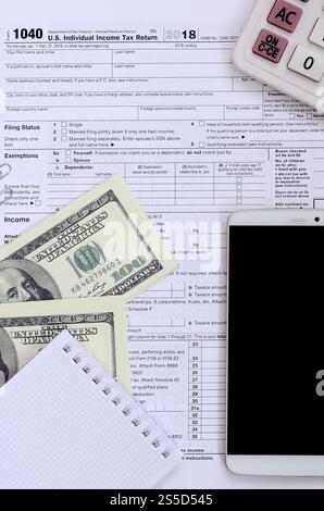 Composizione delle voci che si trovano sul formulario fiscale 1040. Banconote in dollari, calcolatrice, smartphone, graffetta e blocco note. Il tempo di pagare le tasse Foto Stock