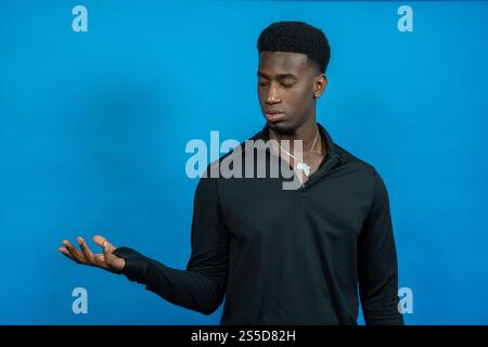 Giovane elegante che mostra qualcosa con la mano che indossa il ciondolo africa su sfondo blu Foto Stock