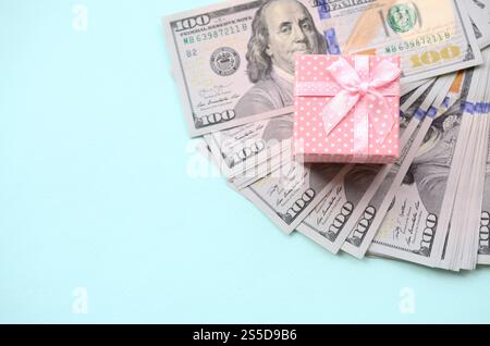 La confezione regalo rosa punteggiata si trova a circa cento banconote da un dollaro su sfondo azzurro. La confezione regalo rosa punteggiata si trova vicino a cento banconote da un dollaro su un blu chiaro Foto Stock