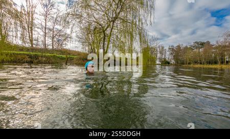 Donna matura che indossa occhiali e un cappello in maglia turchese Wild Swimming in una mattina d'inverno, Regno Unito Foto Stock