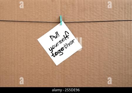Mettetevi insieme. La nota è scritta su un adesivo bianco appeso a un clothespin su una corda su uno sfondo di cartone marrone Foto Stock