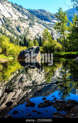 Una grande roccia si trova nel mezzo di un fiume, circondato da alberi. L'acqua è calma e limpida, riflettendo il paesaggio circostante. La scena è la pace Foto Stock
